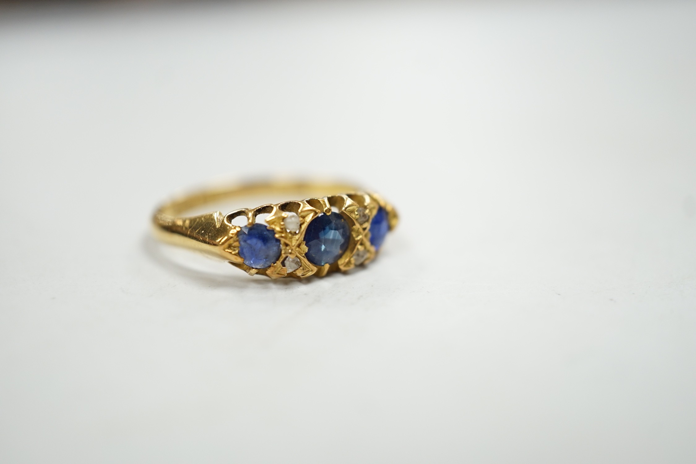 An Edwardian 18ct gold and graduated three stone sapphire set half hoop ring, with four stone rose cut diamond chip spacers, hallmarked for Birmingham, 1906, size P/Q, gross weight 3.2 grams.